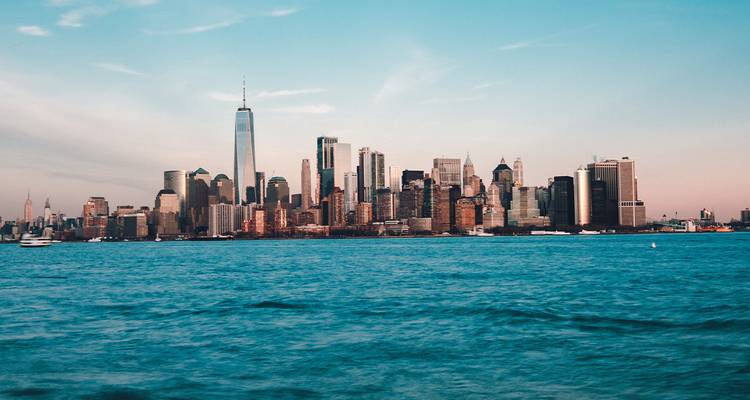 New York City skyline glows in soft evening light across the Hudson River with a pastel sky.