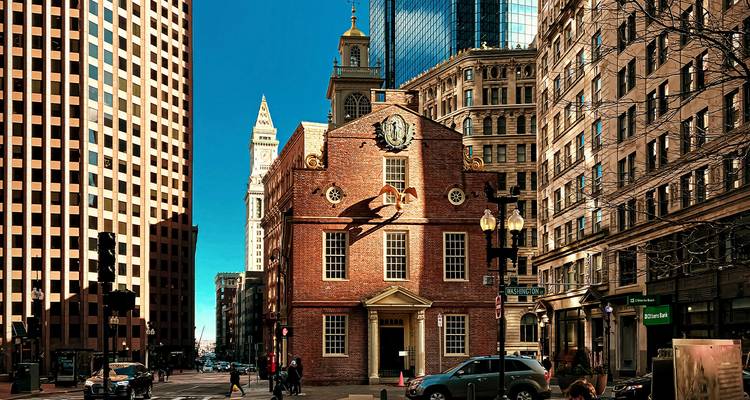 Historic red-brick Old State House nestled among modern skyscrapers under a clear blue sky.