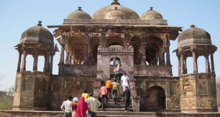 Local visitors climb steps of an old sandstone cenotaph with domed chhatris.