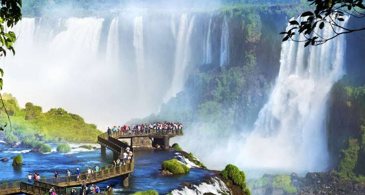 Crowded boardwalk extending toward massive curtain of Iguazu waterfalls with spray all around