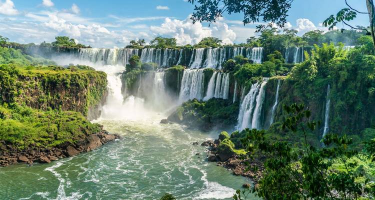 Wide angle view of multiple tiers of Iguazu Falls crashing into green river below
