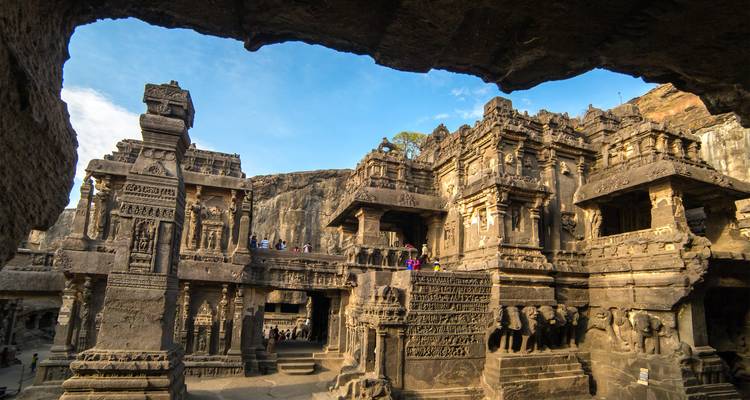 Monolithic stone temples and richly carved pillars form the impressive Kailasa complex within a sunlit rock face.
