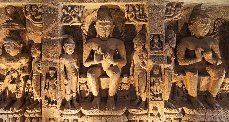 Detailed stone carvings of seated Buddhas and attendants adorn the interior walls of an ancient cave temple.