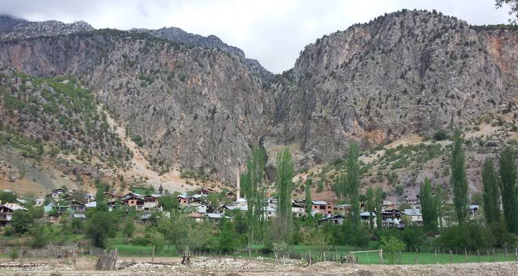 Petit village turc niché au pied de falaises rocheuses imposantes avec de hauts peupliers élancés.
