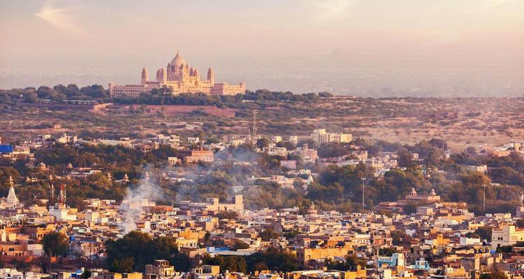 Elevated twilight view over sprawling Jodhpur city with Umaid Bhawan Palace on distant ridge.