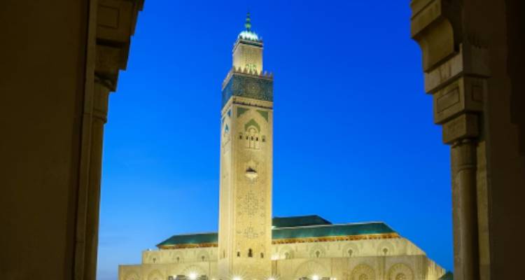 Hassan II Mosque minaret illuminated against a deep blue evening sky.