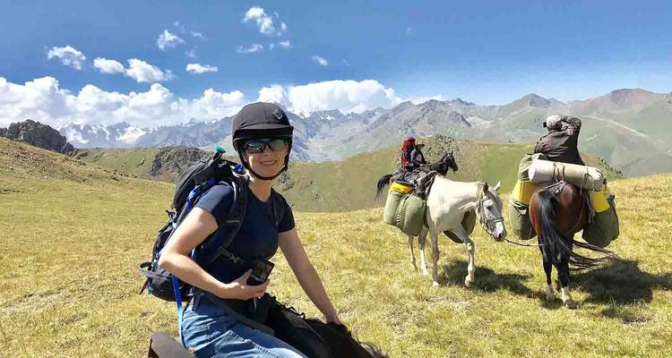 Riders on an open alpine meadow pause with backpacks and helmets under a bright sky.