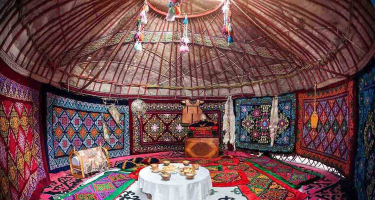 Vibrantly decorated interior of a traditional Kyrgyz yurt with colorful textiles and low dining table.
