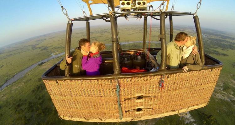 Two couples share kisses while floating high above the savanna in an open hot-air-balloon basket.