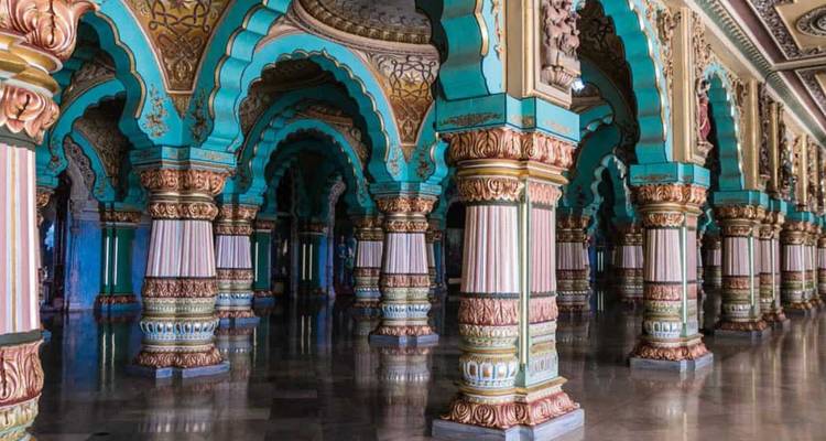 Kunstvolle bemalte türkisfarbene und goldene Bögen und Säulen säumen den polierten Boden im Inneren des Mysore-Palastes.