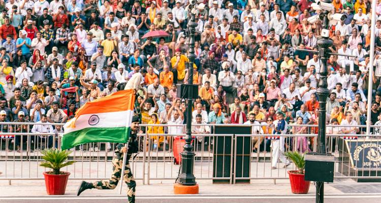 Indian border guard sprinting with the national flag during the Wagah border ceremony before a huge crowd.