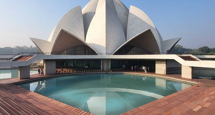 Modern white-petaled Lotus Temple reflected in a turquoise pool under clear skies in Delhi.