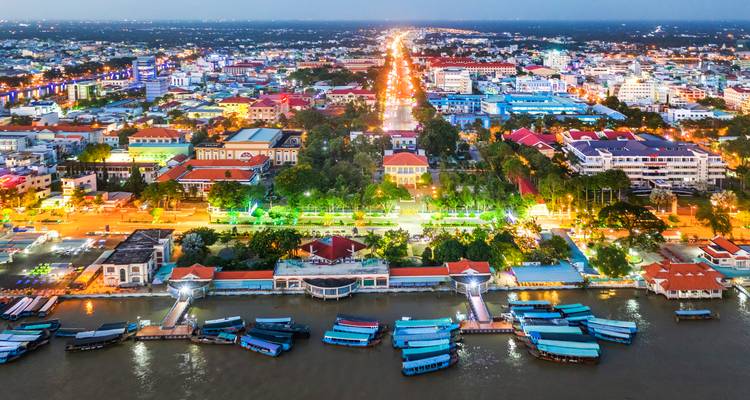 Night aerial of Phnom Penh riverside with illuminated boulevard and boats docked along Mekong.