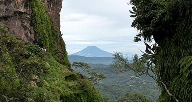 Green canyon walls draped in vegetation open to a distant volcanic peak on the horizon.