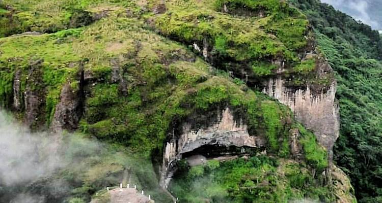 Misty green cliff with a cavernous opening and winding trail leading upward.