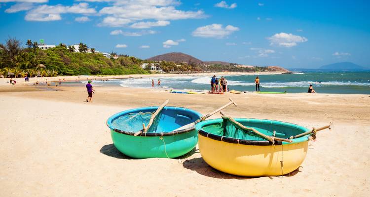 Sunny tropical beach with traditional round basket boats on the sand and swimmers in the surf.