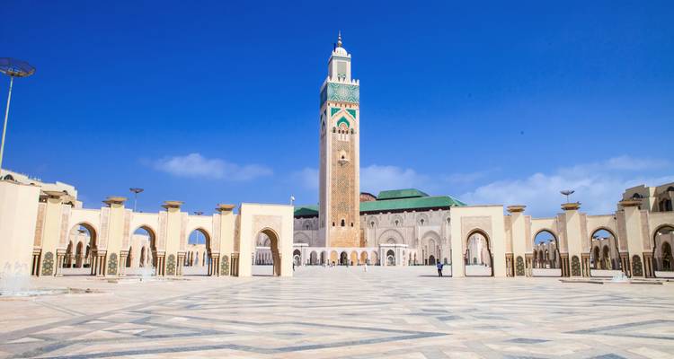 Vast marble courtyard leading to the towering Hassan II Mosque against a deep-blue sky.