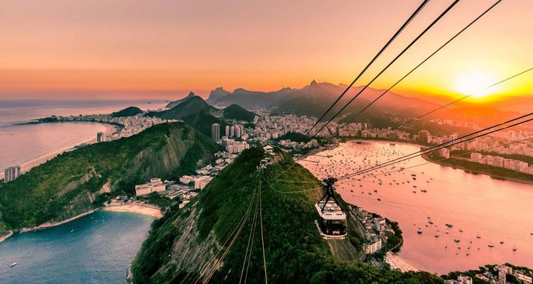 Sunset over Rio de Janeiro with cable cars ascending Sugarloaf Mountain and golden light bathing the coastline.