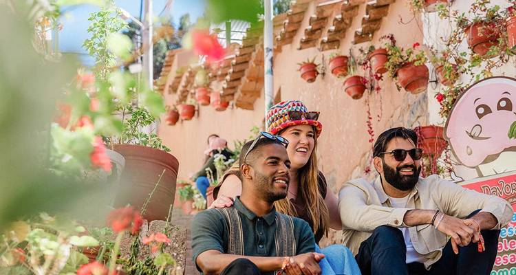 Friends sit on colourful Cusco street steps decorated with flower pots, laughing together.