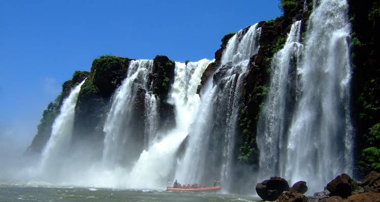 Powerful wall of water plunges into mist with a small adventure boat dwarfed below at Iguazu.