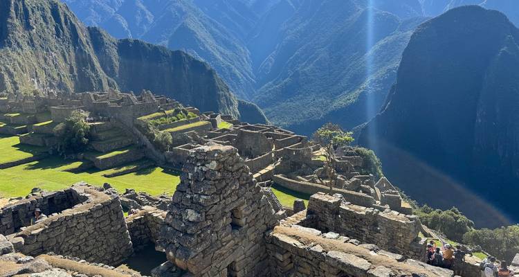 Stone ruins of Machu Picchu perched on an Andean ridge with dramatic mountains and sunlight shaft.
