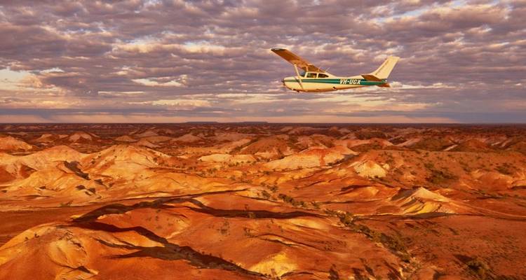 Light aircraft soaring above the vivid ochre formations of the Painted Desert near Coober Pedy.