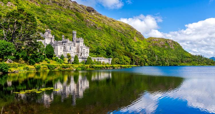 Castle-like Kylemore Abbey mirrored in a tranquil lake against green mountains and blue sky