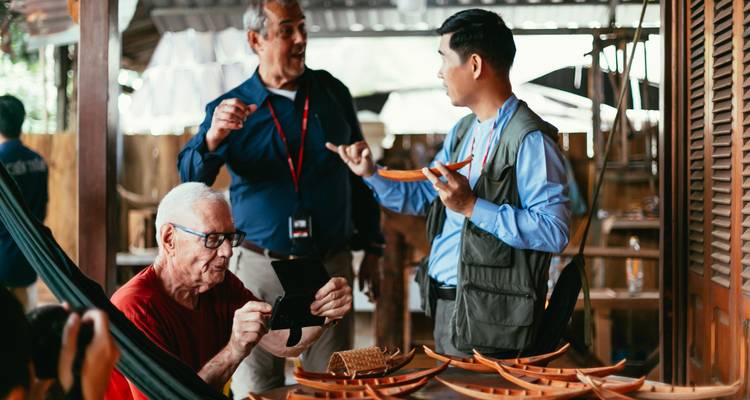 Voyageurs discutant avec un artisan local à propos d'objets d'artisanat en bois dans un atelier ouvert.