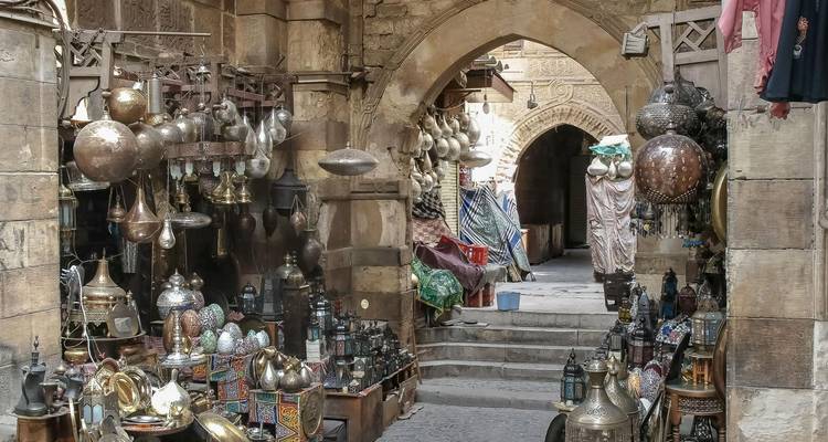Narrow stone archway leads into a bustling souk filled with ornate brass lamps, hookahs and metalware.
