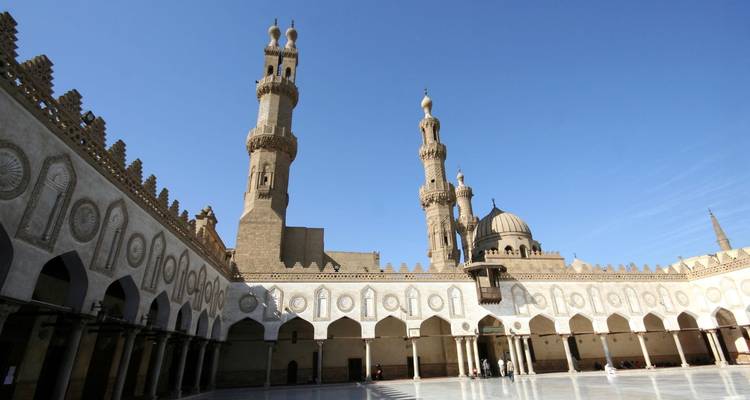 Open courtyard of Al-Azhar Mosque with elegant arches and twin minarets under a clear blue sky.