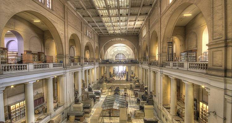 Grand hall of the Egyptian Museum with towering arches, skylights and rows of ancient artifacts.