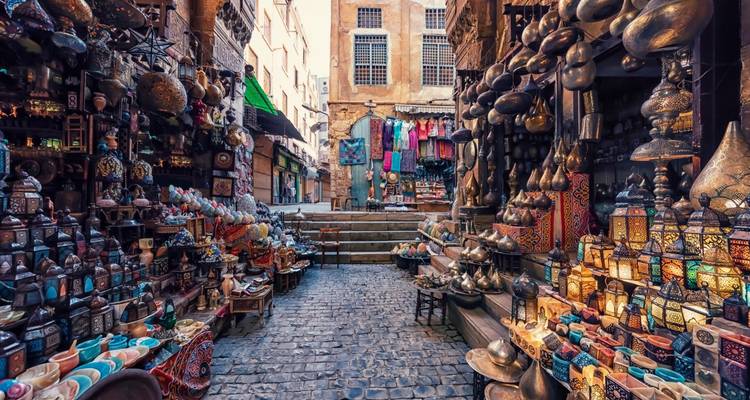 Colorful, lamp-filled alleyway of a traditional Cairo bazaar with cobblestone path and vibrant textiles.
