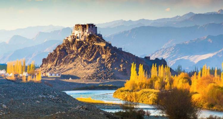 Dramatic fortress-topped hill beside river and yellow poplars against distant Himalayas.