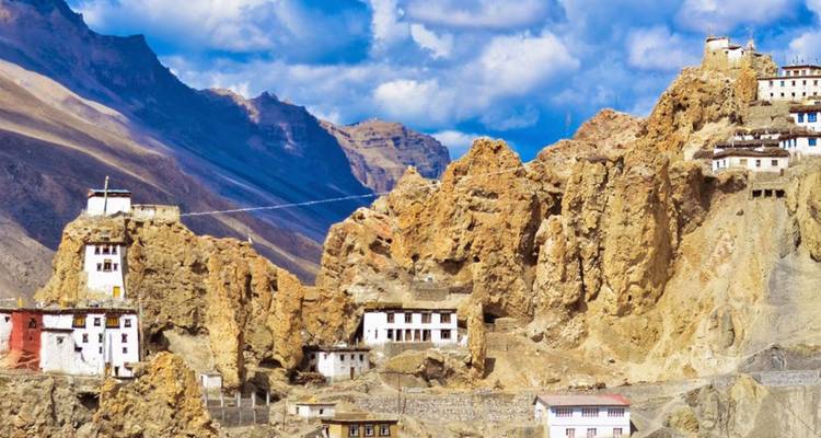 Cliff-hugging monasteries and white stupas built into golden mountains under blue sky.
