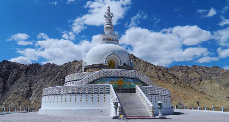 White Shanti Stupa rising against rocky hills under bright blue sky and clouds.