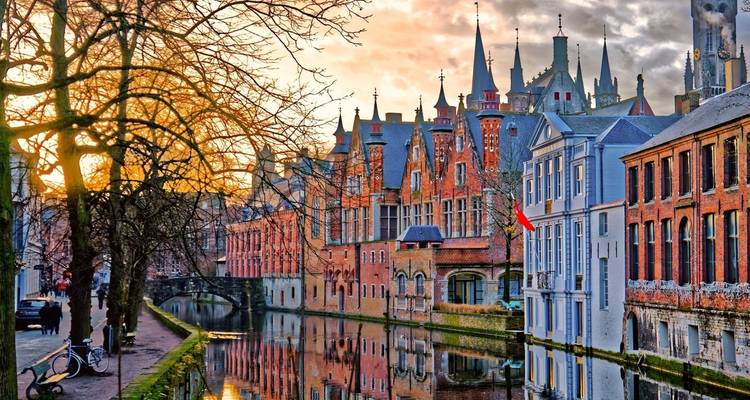 Romantic sunset over Bruges’ medieval canal lined with spired brick buildings reflected in still water.