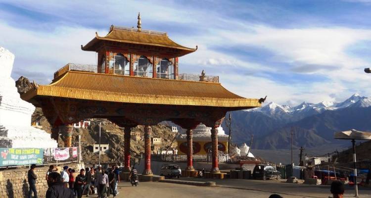 Golden-roofed Tibetan-style entrance gate with distant snow peaks and visitors gathered below.
