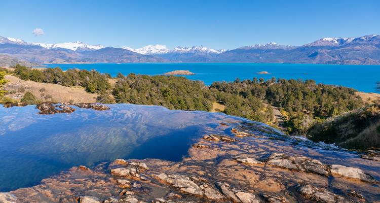 Natuurlijk infinity pool met uitzicht op een helder turquoise Patagonisch meer en besneeuwde toppen.