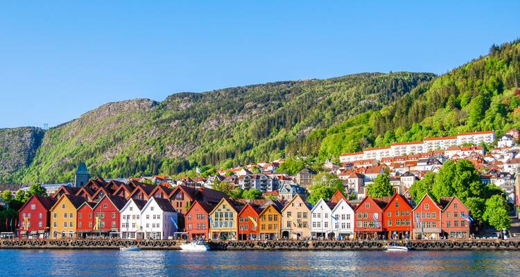Iconic Bryggen row of colorful wooden warehouses reflected in calm water against green hills