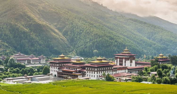 Uitgestrekt dzong-complex met gouden daken gelegen in een weelderige groene vallei onder mistige heuvels