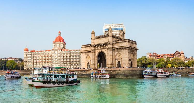 Gateway of India arch and the Taj Mahal Palace Hotel with tour boats on Mumbai Harbour's turquoise waters.