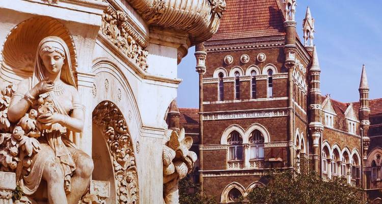 Close view of a white marble fountain statue with intricate colonial architecture of Mumbai in the background.