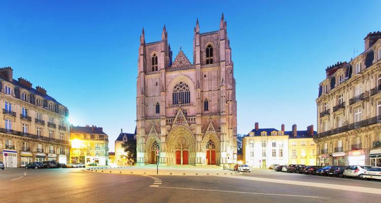La cathédrale de Nantes illuminée s'élève au-dessus d'une place animée à l'heure bleue.