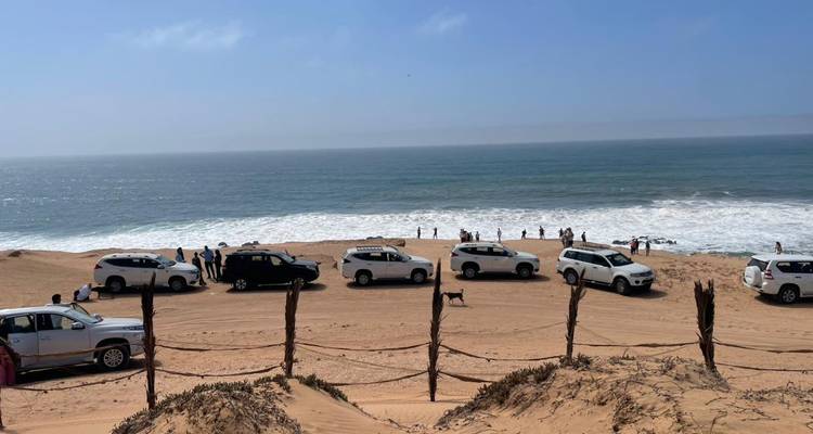 Line of white 4x4 vehicles parked on sandy beach facing a crashing ocean surf.