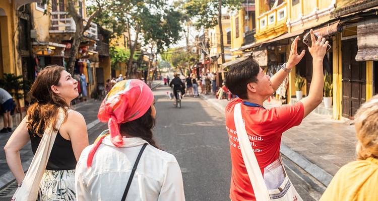 Führer im roten Hemd zeigt Sehenswürdigkeiten entlang der belebten Straße mit gelben Wänden in der Altstadt von Hoi An.