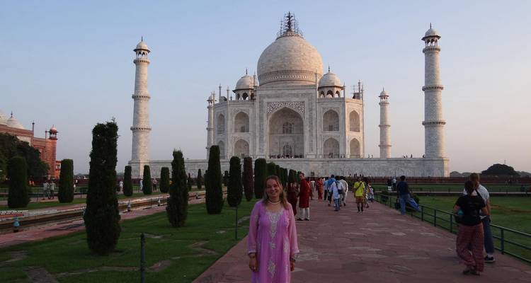 Visitor in pink dress poses on the Taj Mahal forecourt at dawn with other tourists around.