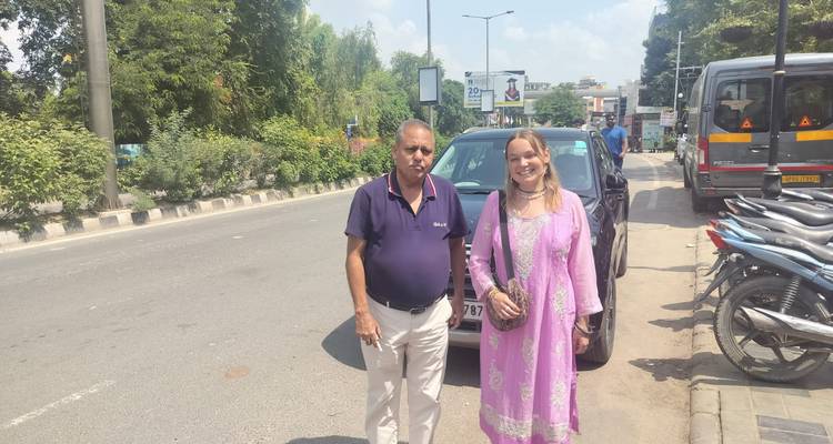 Tourist and driver stand beside a parked car on a sunny city street in Agra.