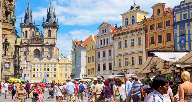 Bustling Prague Old Town Square filled with tourists beneath colorful baroque buildings and the twin spires of Tyn Church.