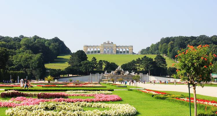 Formal flower gardens of Schönbrunn Palace with the Gloriette monument perched on a hill in the distance.