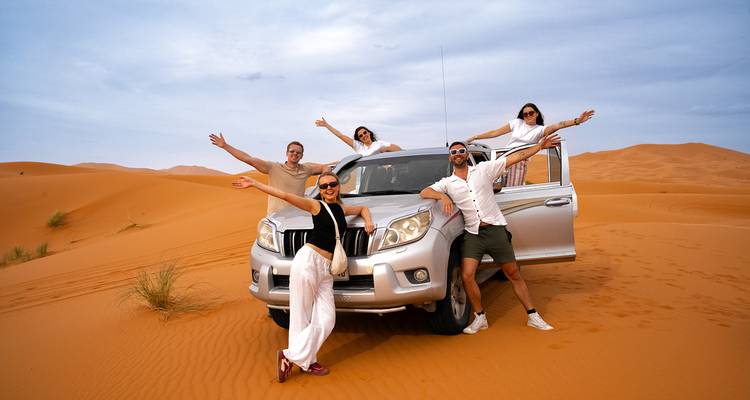 Des amis posent avec un véhicule tout-terrain au milieu des vastes dunes du Sahara sous un ciel pâle.